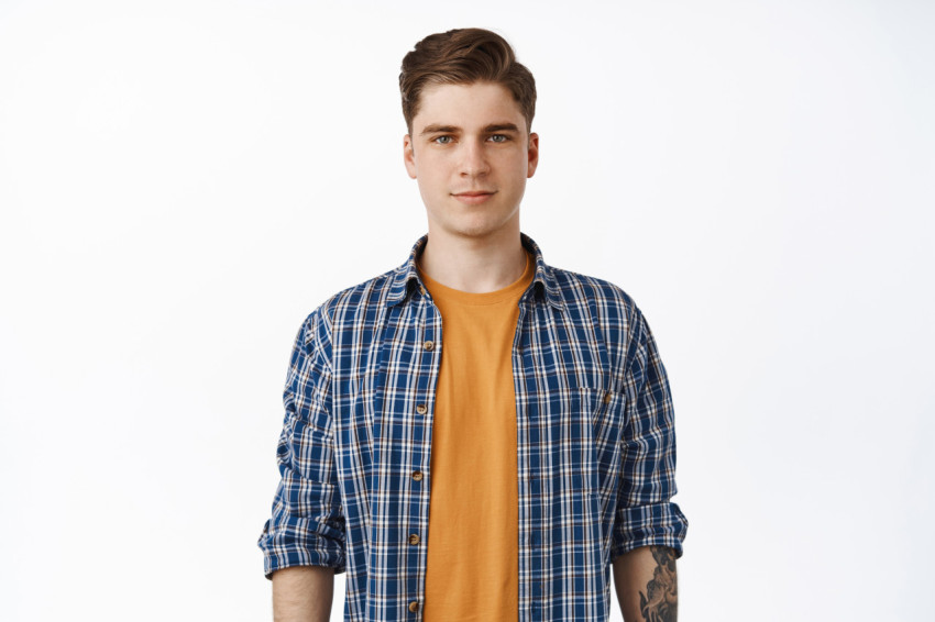 Portrait of young candid man, student boy with clean face, relaxed facial expression and casual smile, checked shirt over t-shirt, summer outfit look, white background